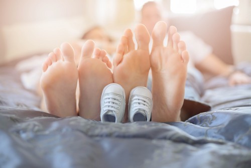 Pregnant mother and future dad feet on bed and little unborn baby shoes
