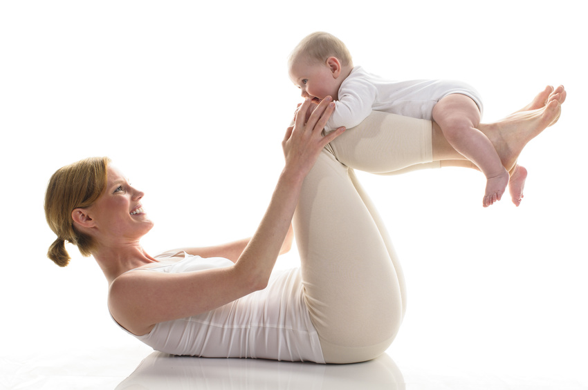 Junge Mutter macht mit ihrer 6 Monate alten Tochter Rueckbildungsgymnastik, isoliert vor weissem Hintergrund. Mama liegt am Boden und hat ihr Baby auf ihren Unterchenkeln liegen.